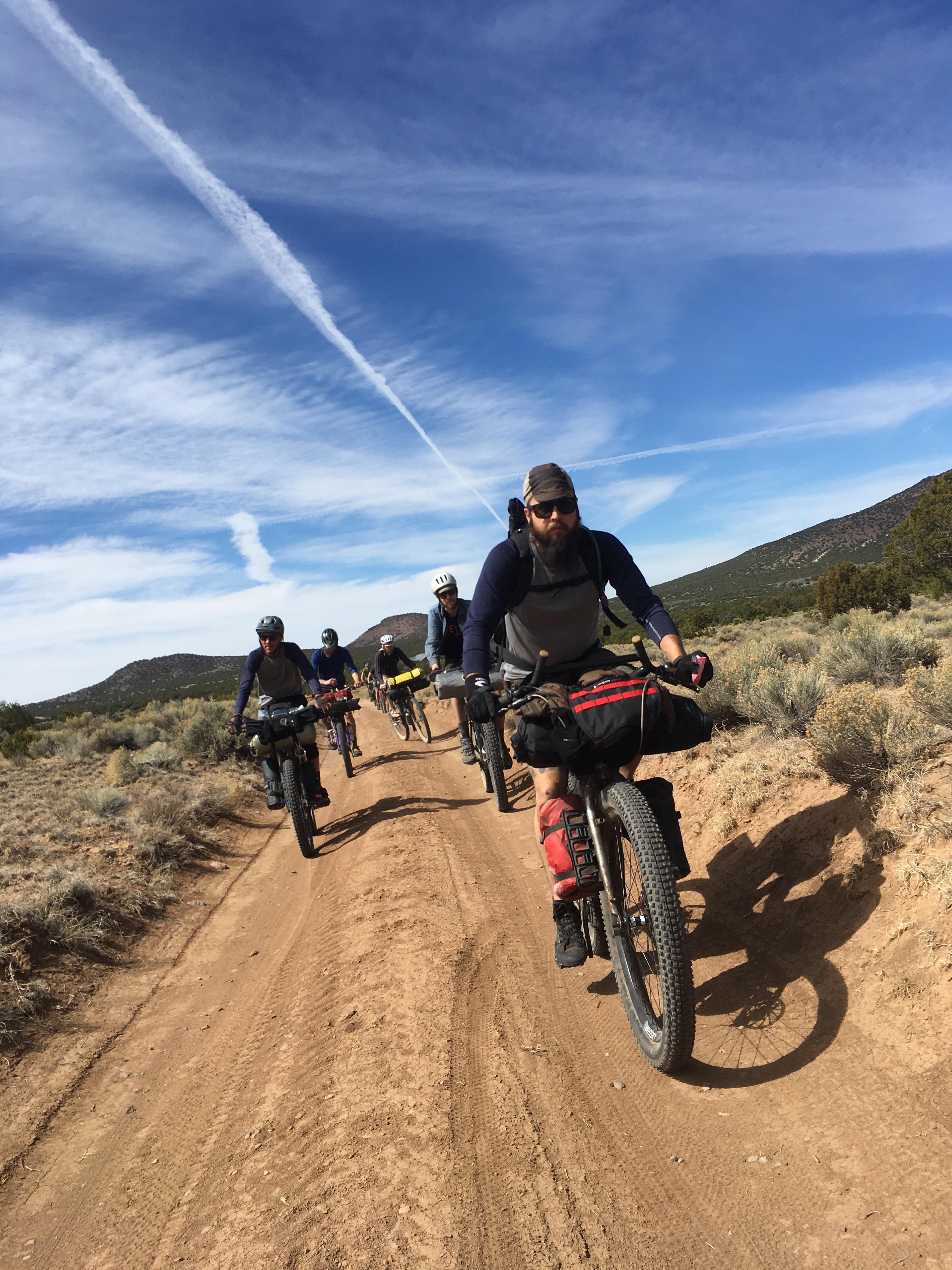 A vertical view of a horizontal photo showing group of cyclist riding down a gravel  desert road