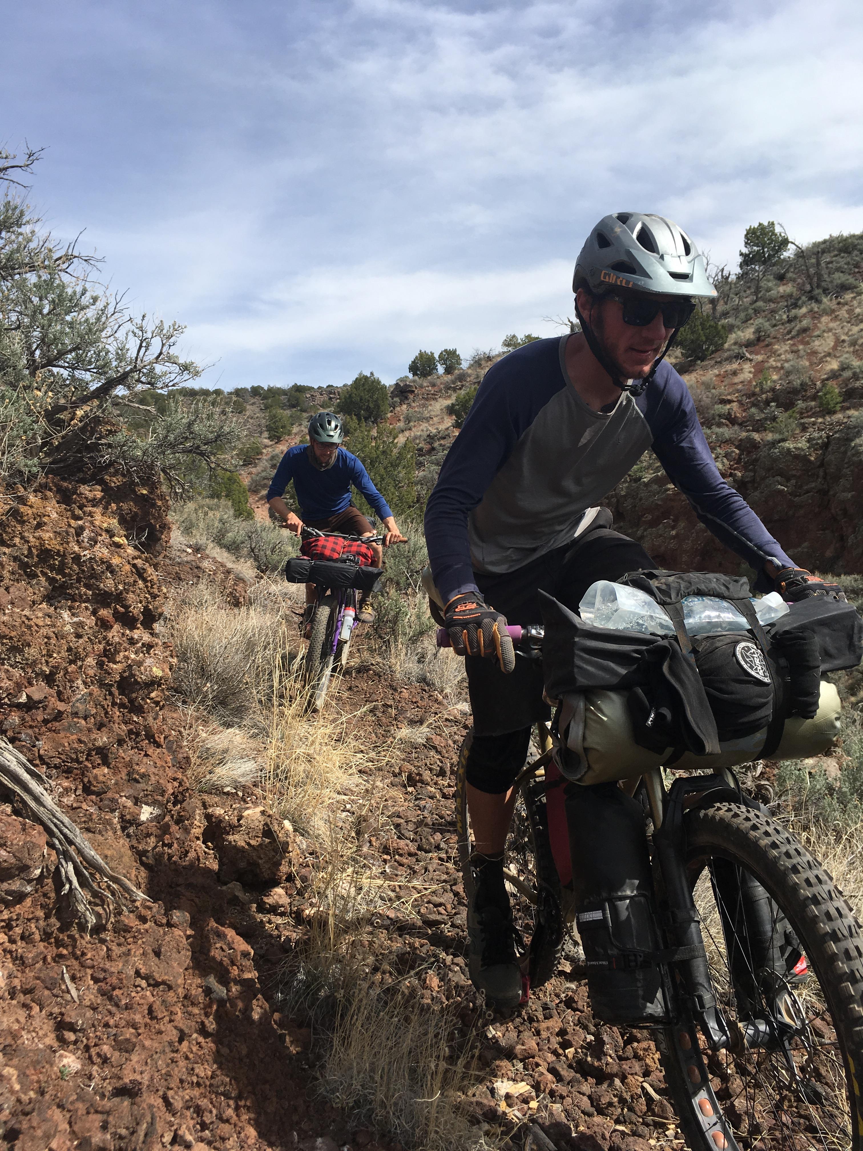 Vertical view of a horizontal front view image showing cyclists with gear loaded bikes on a rocky desert trail
