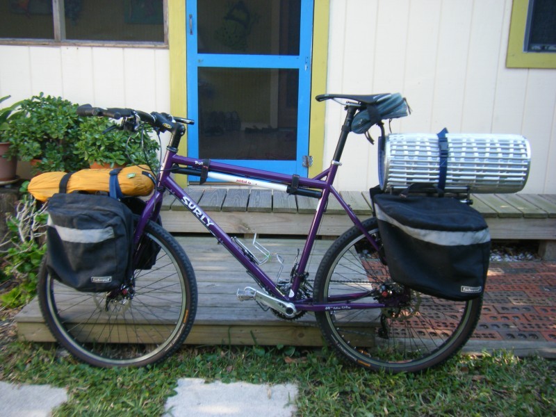 Left side view of a purple Surly Troll bike, loaded with gear, parked in front a wood porch of a house