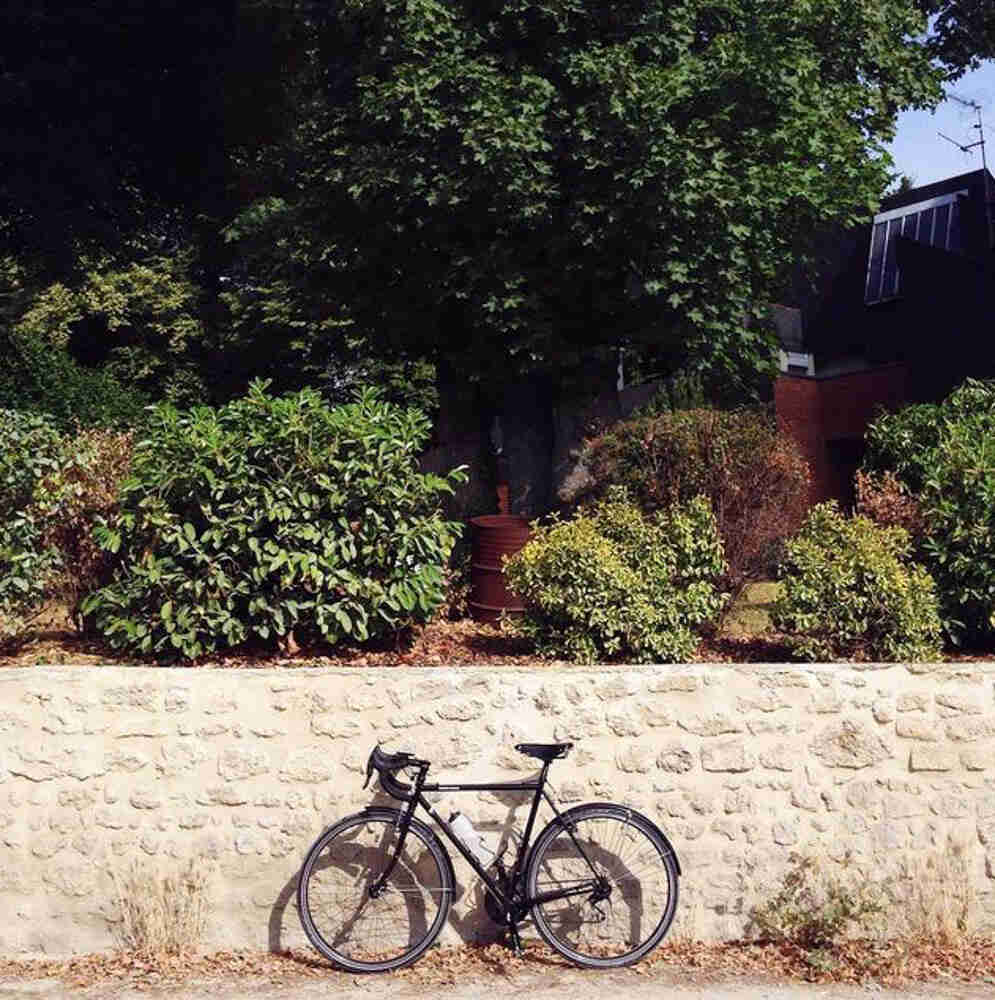 Left side view of a black Surly bike, leaning against a stone wall, with bushes on the ledge above