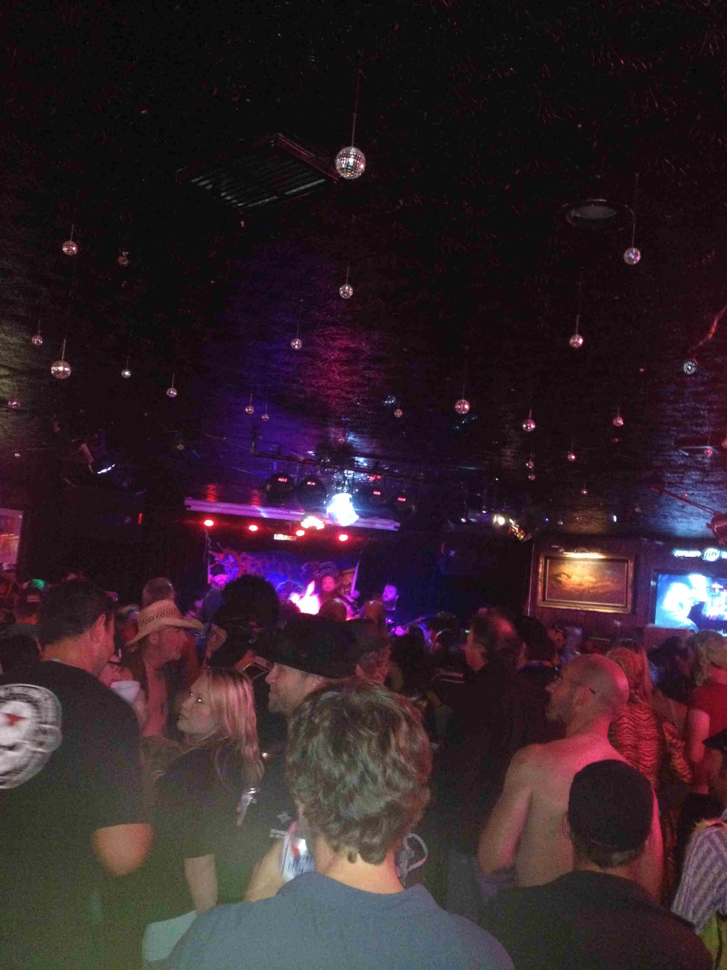 Rear view from the back of a dimly lit room, with people watching a band that's on stage