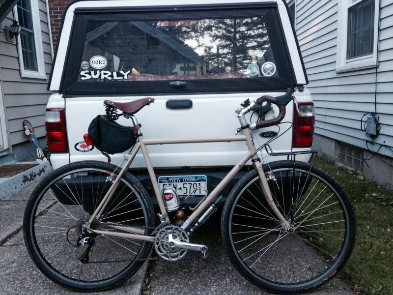Right side view of a Surly Long Haul Trucker bike, leaning against the tailgate of a pickup truck, parked on a driveway