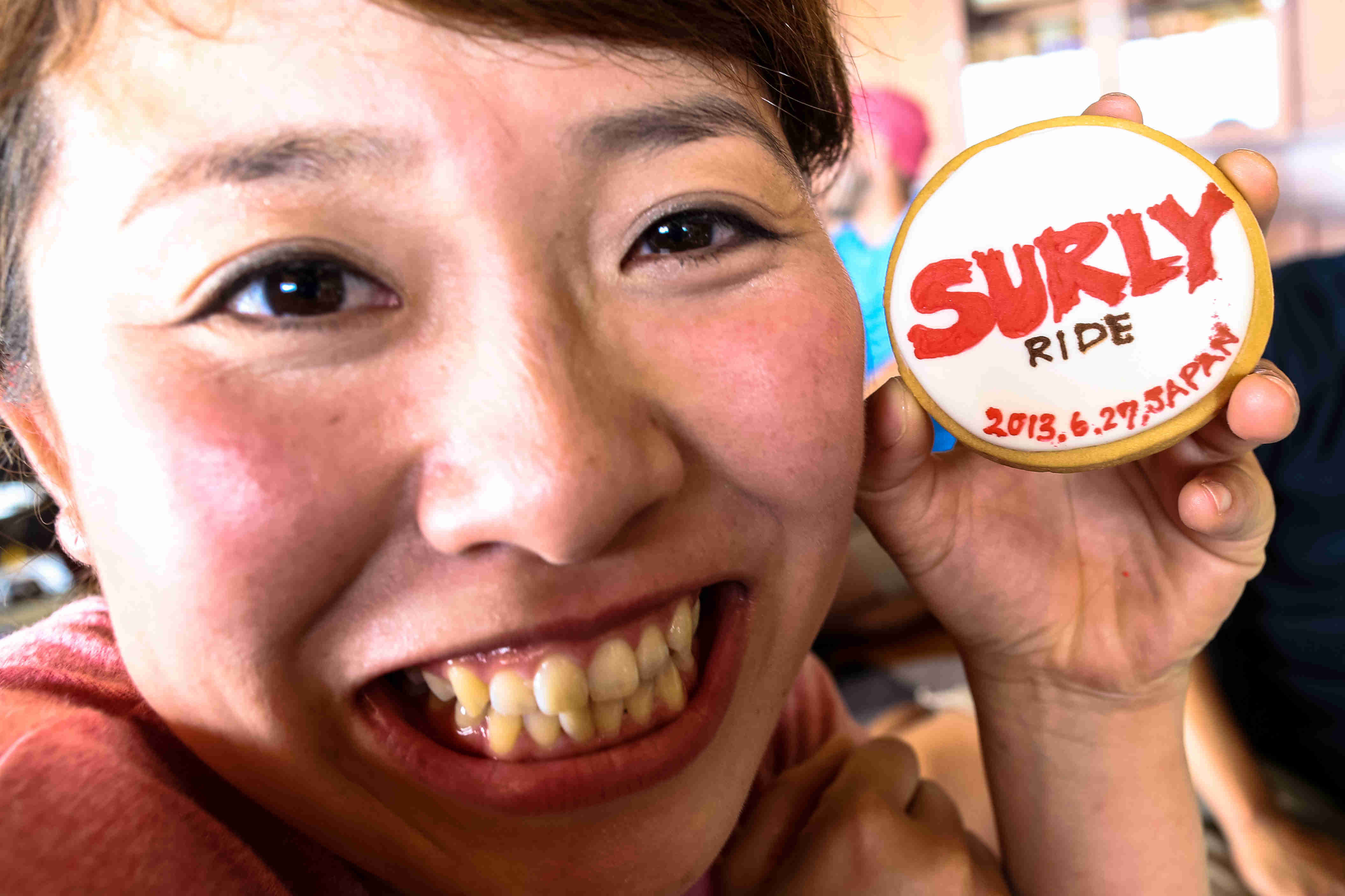 Headshot of a smiling person, holding up a cookie with, Surly Ride - 2013.6.27, Japan, decorated on it, near their face