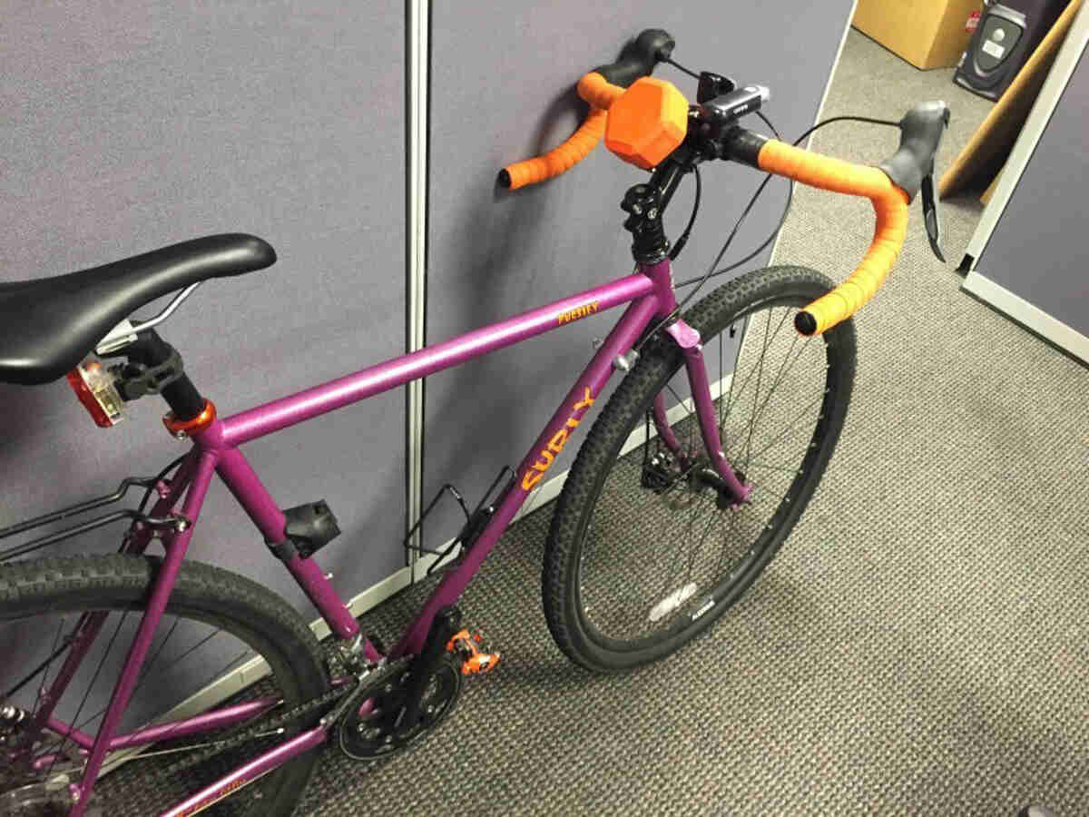 Downward, right side view of a purple Surly Straggler bike, parked against a cubicle wall, in an  office