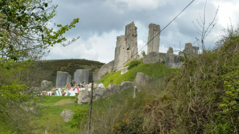Upward view of a hill with a crumbling castle on top, with tents below at the base of the hill