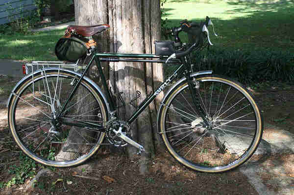 Right side view of a green Surly Cross Check bike, leaning against the base of a tree with grass in the background