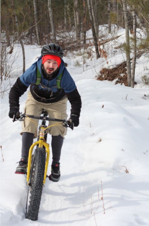 Front view of a cyclist, riding a yellow Surly fat bike, on a snow covered trail in the woods