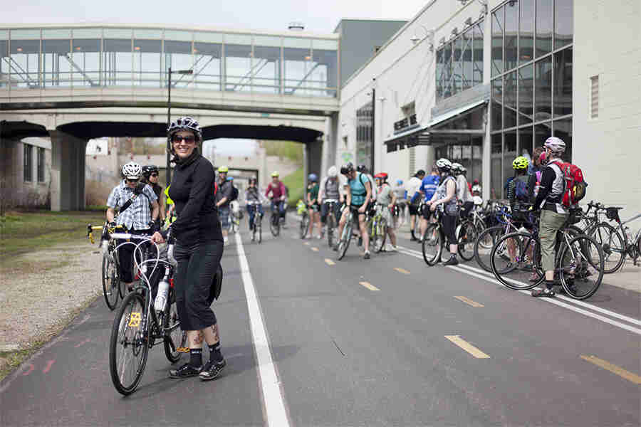 Front view of a cyclist standing with their Surly bike, on the side of a bike street, with a group of cyclists behind