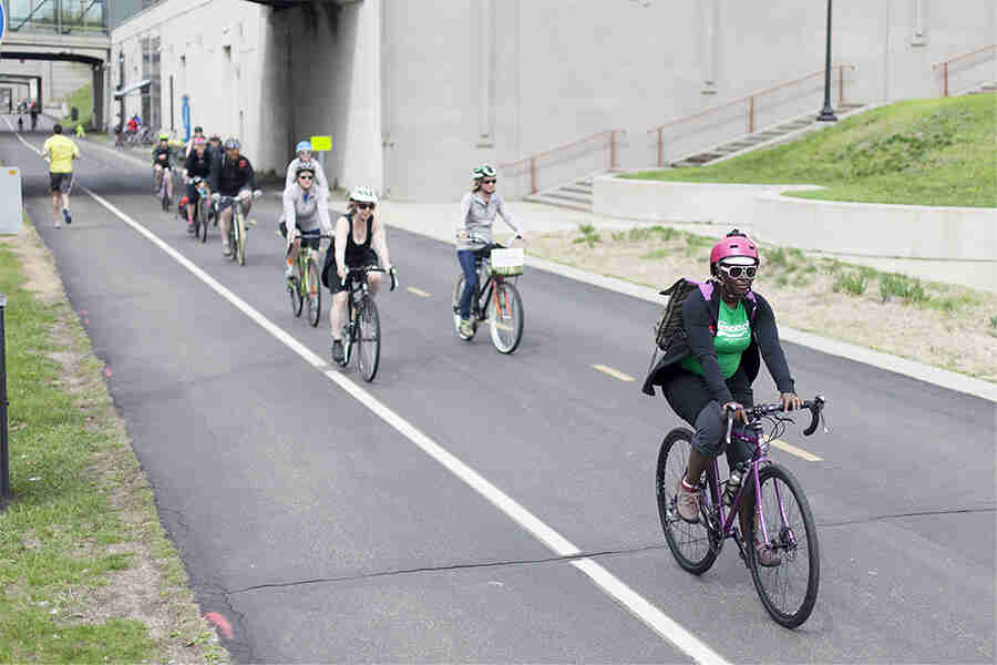 Front, right side view of cyclist, riding a purple Surly bike, on a paved bike street with other cyclists riding behind