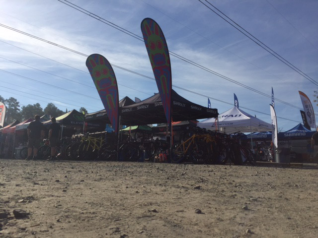 Ground level view from a gravel lot in front of a row of Surly canopies, loaded with bikes underneath