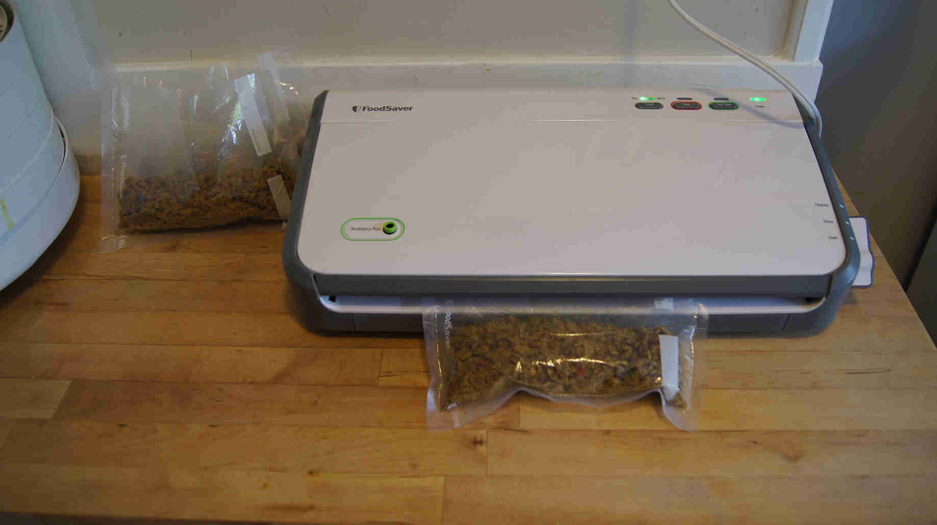 Soup ingredients in a plastic bag being sealing in a food vacuum sealer, on top of a wood countertop