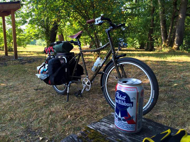 Right side view of a Surly Bike Dummy bike, parked in a grass field with trees behind, and a beer can in the forefront