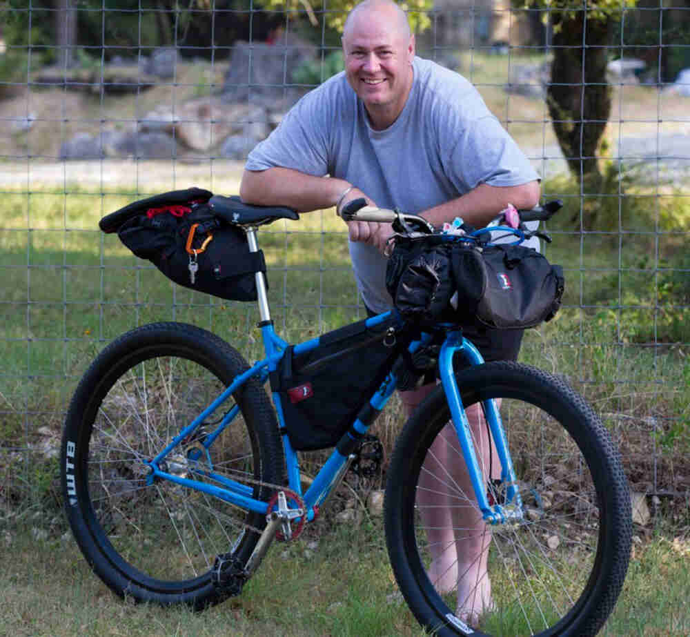 Right side view of a blue Surly bike with gear packs, with a cyclist leaning over from the left side
