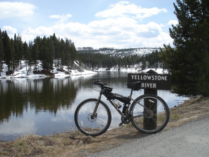 Left side view of a Surly bike with gear, leaning against a post on a grassy bank of the Yellowstone river