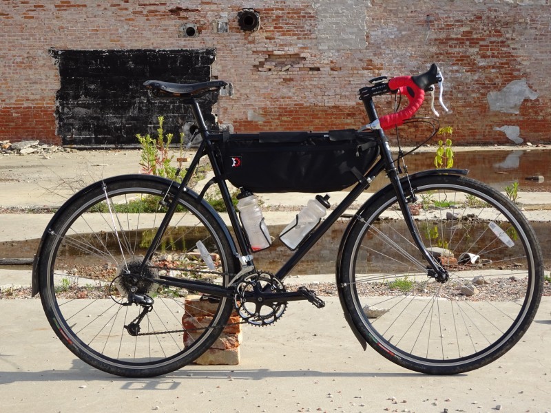 Right side with of a black Surly bike, parked on a concrete lot, with a brick building wall in the background