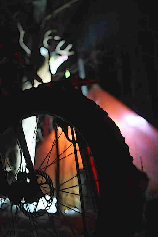 Close up view of a fat bike wheel, with a blurred tent behind, in the woods at night