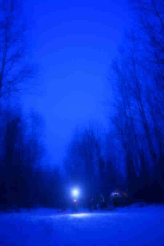 Blurry blue saturation view of a campsite in the snow with a bright light, in the woods