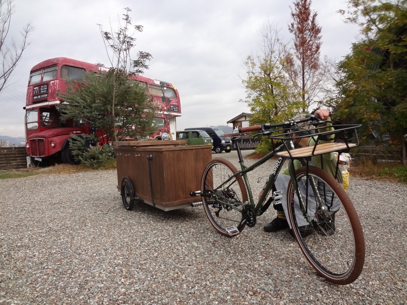 Front right side view of a Surly bike with a wood trailer hitched behind, with a person squatting near the front