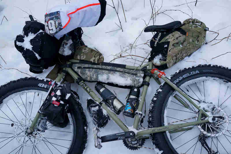 Left side view of a Surly fat bike, loaded with gear, laying on it's side in the snow