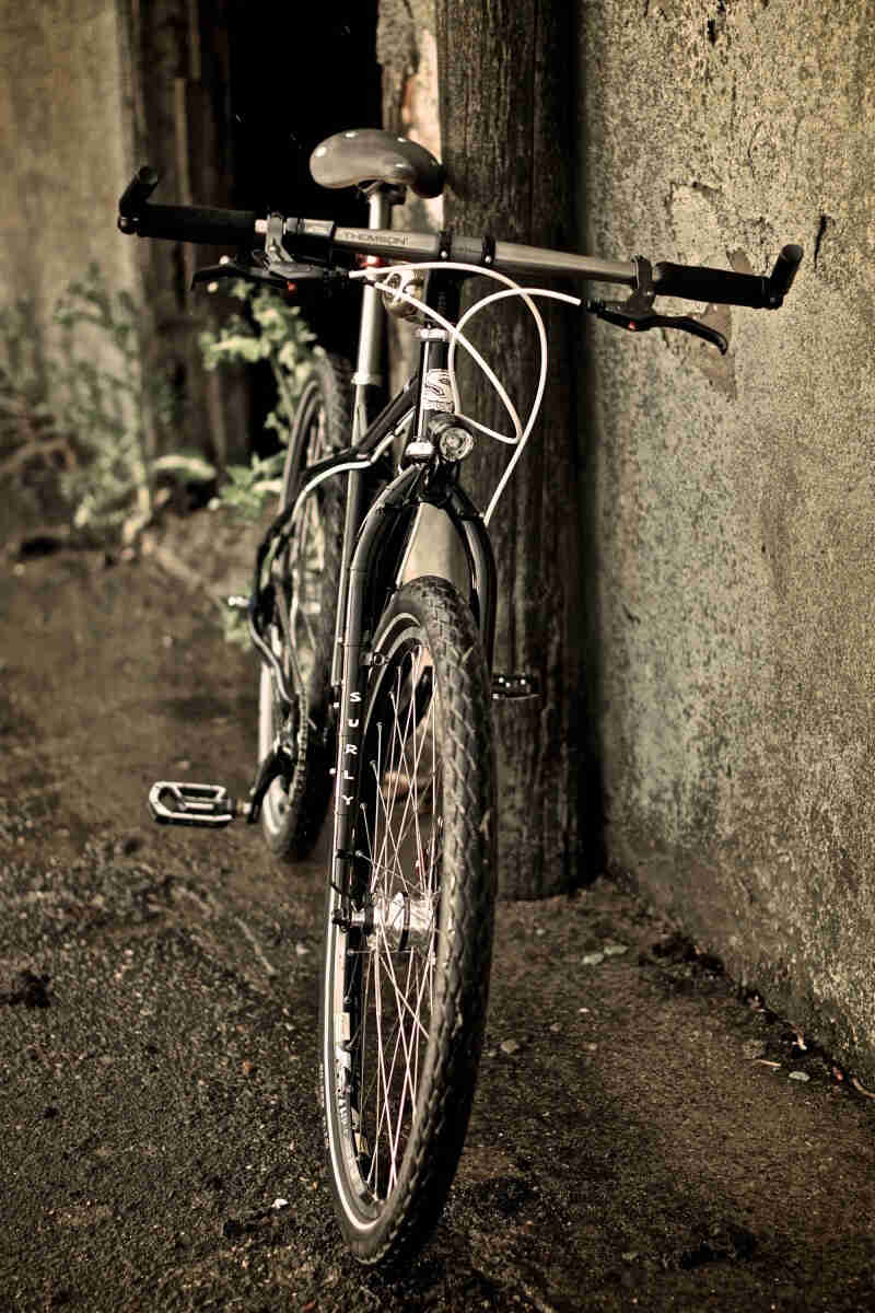 Front view of a black Surly bike, leaning on a concrete wall with a doorway on it