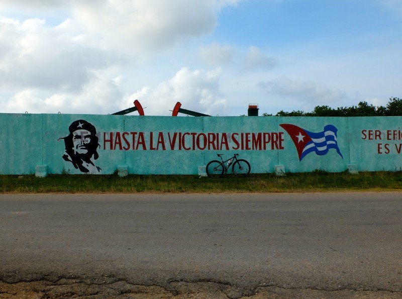 Right side view of a bike, leaning on a turquoise wall, with painted words, Cuban flag and Che Guevara on it