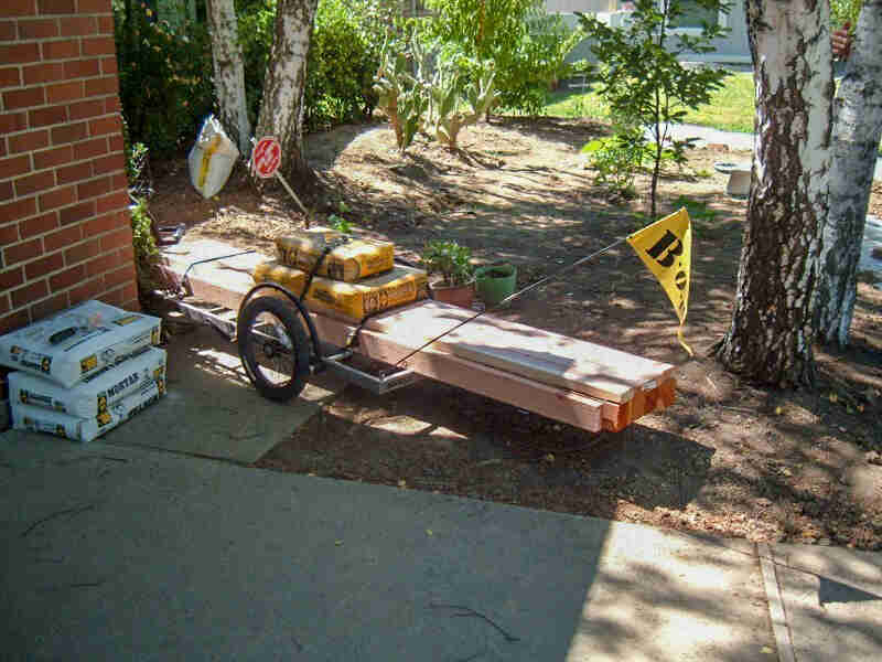 Rear view of a bike trailer, loaded with building materials, parked next to a brick wall of a house