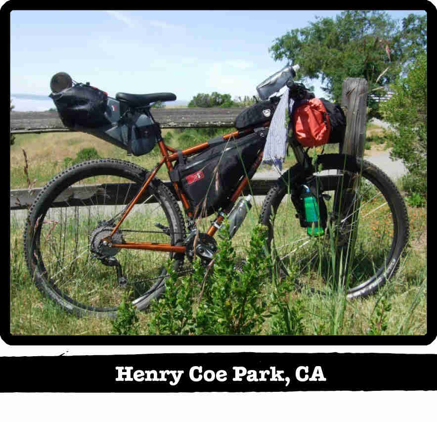Right side view of a Surly bike, loaded with gear, in the weeds leaning on a wood fence - Henry Coe Park, CA tag below image