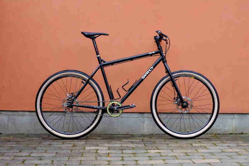 Right profile of a black Surly bike, on a sidewalk, in front of a peach colored wall