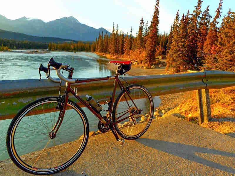 Left side view of a Surly bike parked on a bridge over a river, with mountains and trees in the background