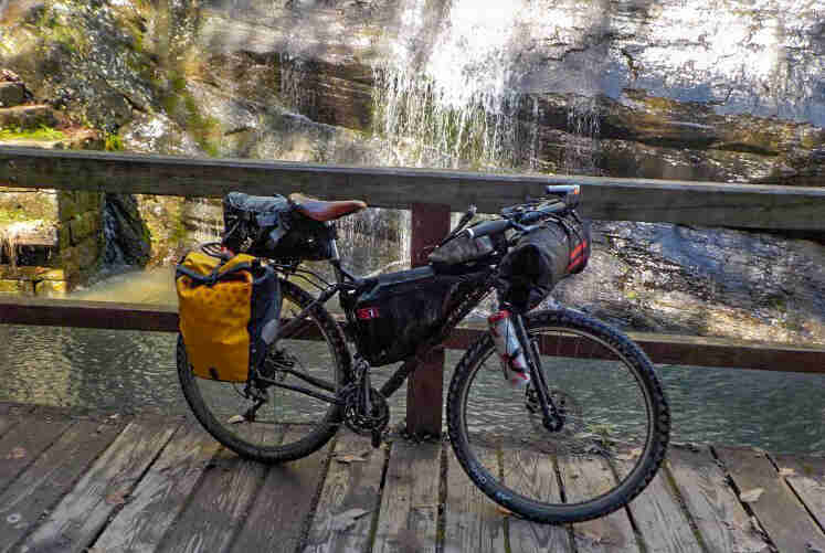 Right side view of a black Surly bike with gear, on a bridge, along the rail, with a waterfall in the background