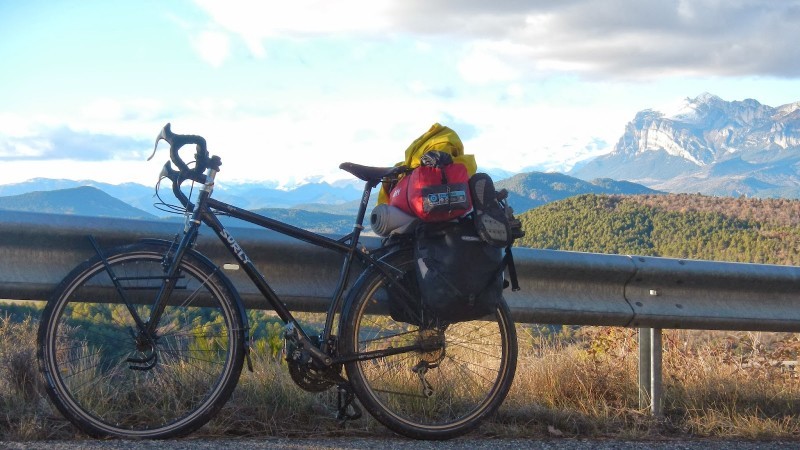 Left side view of a Surly Ogre bike, with a loaded rear rack, leaning against a road guardrail in the mountains