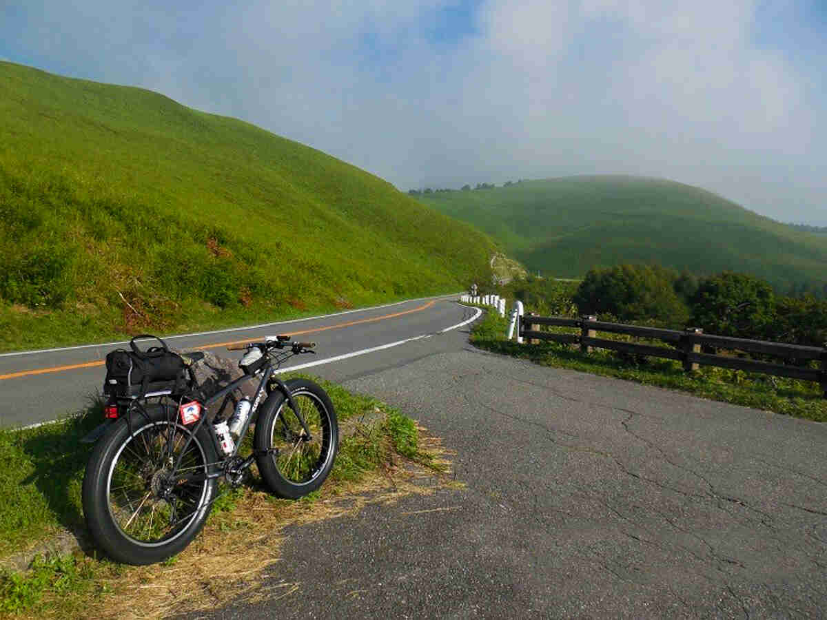 Right side view of a black Surly bike with gear packs, parked along the side of a paved road with green hills behind