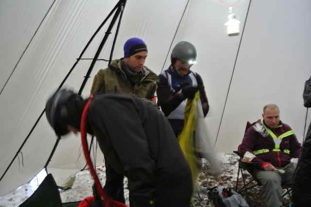 People wearing winter outerwear, sitting and standing inside a teepee tent
