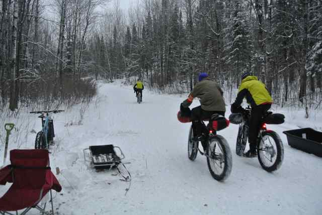 Rear view of three cyclists, wearing winter attire, riding their Surly fat bikes down a snow covered trail in the woods
