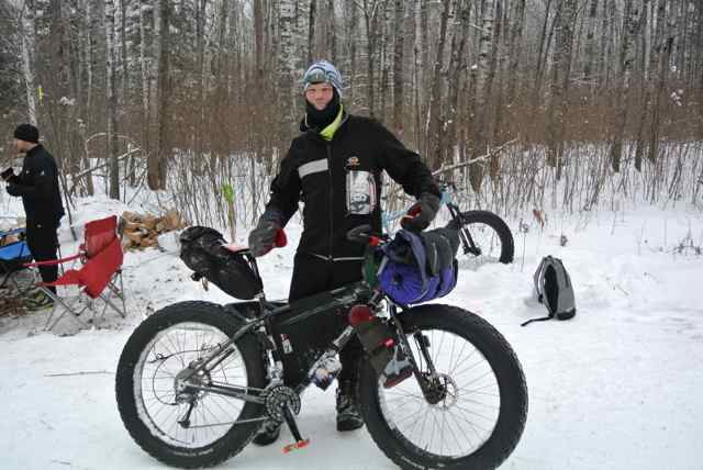 Right side view of a Surly fat bike, with a cyclist wearing winter attire standing behind , on snowy ground