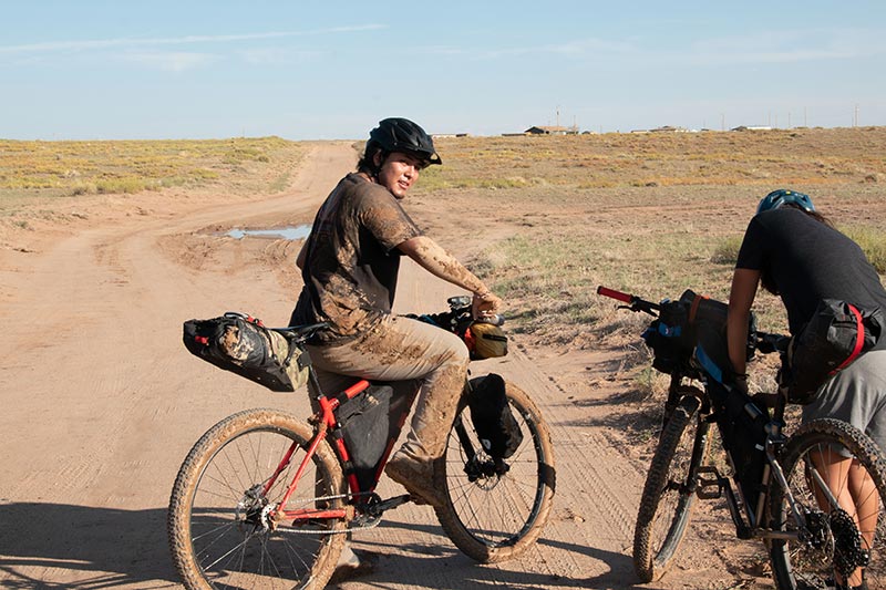 Two mountain bikers taking a break on gravel road, one digging in framepack