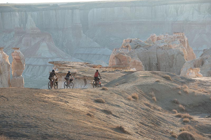 Three mountain bikers riding near edge of canyon with view of opposite facing cliff