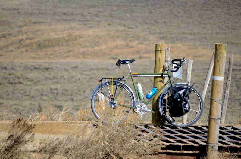 Right profile of a Surly bike, green, parked on a steel crossover for a gravel road, in the grassy plains