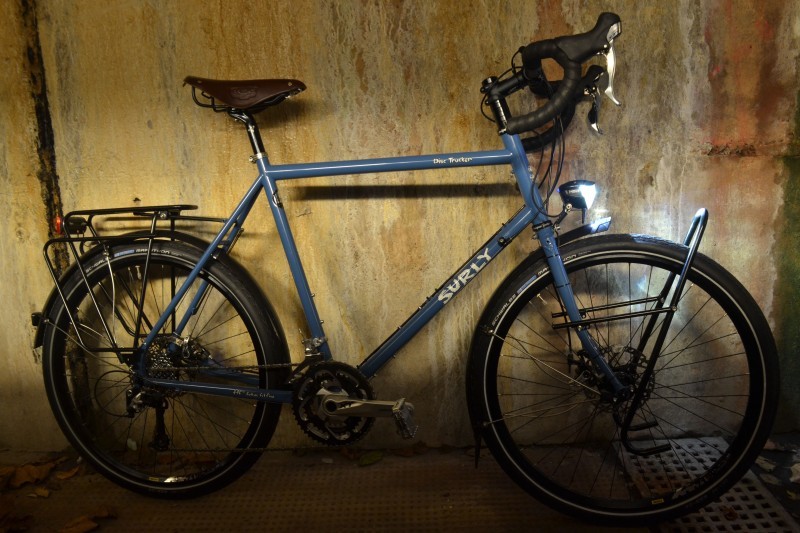 Right side view of a light blue Surly Disc Trucker bike, parked along a concrete wall