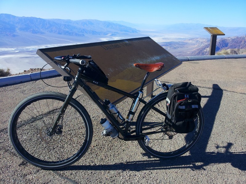 Left side view of an olive Surly ECR bike, leaning against a sign on a scenic overlook, with mountains in the background