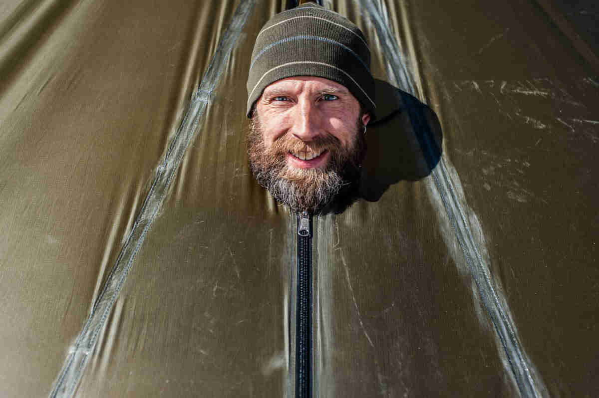 Front view of a smiling person with their head sticking out of a zipped up tent