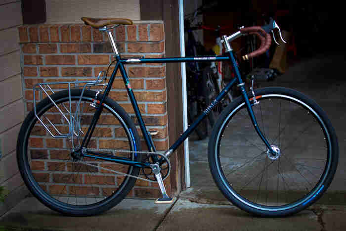 Right side view of a green Surly Travelers Check bike, parked in front a brick wall and an open garage door