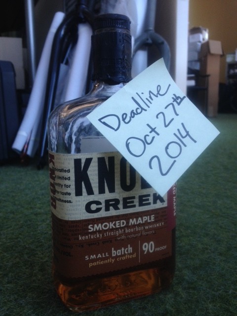 A bottle of Knob Creek smoked maple whisky, with a Post-It note that shows, Deadline Oct 27th 2014, stuck to it