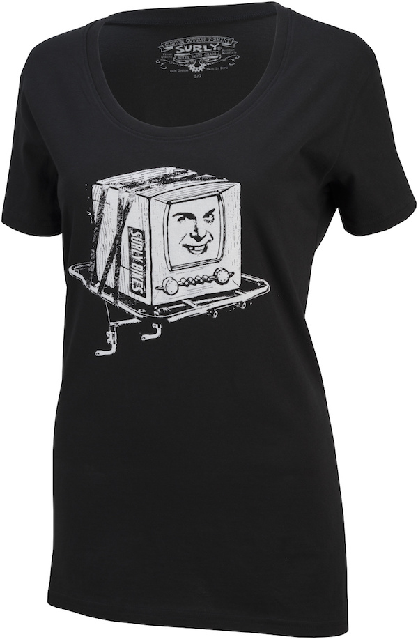 Front view of a black Surly T-shirt with a picture of a TV with a Surly bike sticker on the side and a face on the screen, sitting on a bike rack