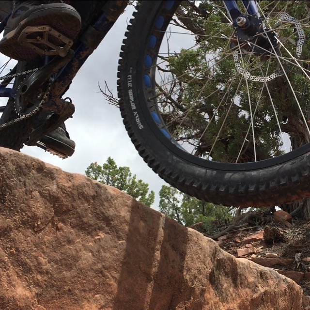 Cropped, upward, right side view of the front wheel of a bike, with Surly Dirt Wizard tires, riding over a rock