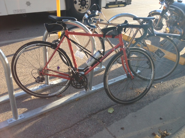 Right side view of a red Surly Disc Trucker bike, leaning against a bike rack on a sidewalk
