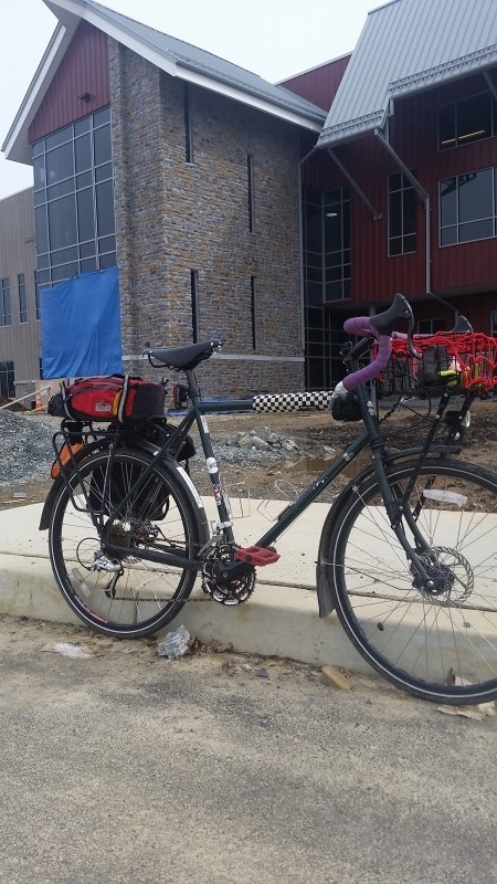 Right side view of a black Surly Disc Trucker bike, loaded with gear, parked along a curb in front of a building
