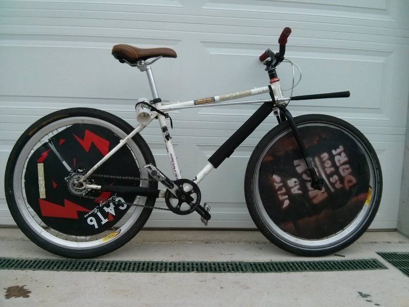Right side view of a white Surly 1x1 bike with wheel covers, parked on the outside of a white garage door