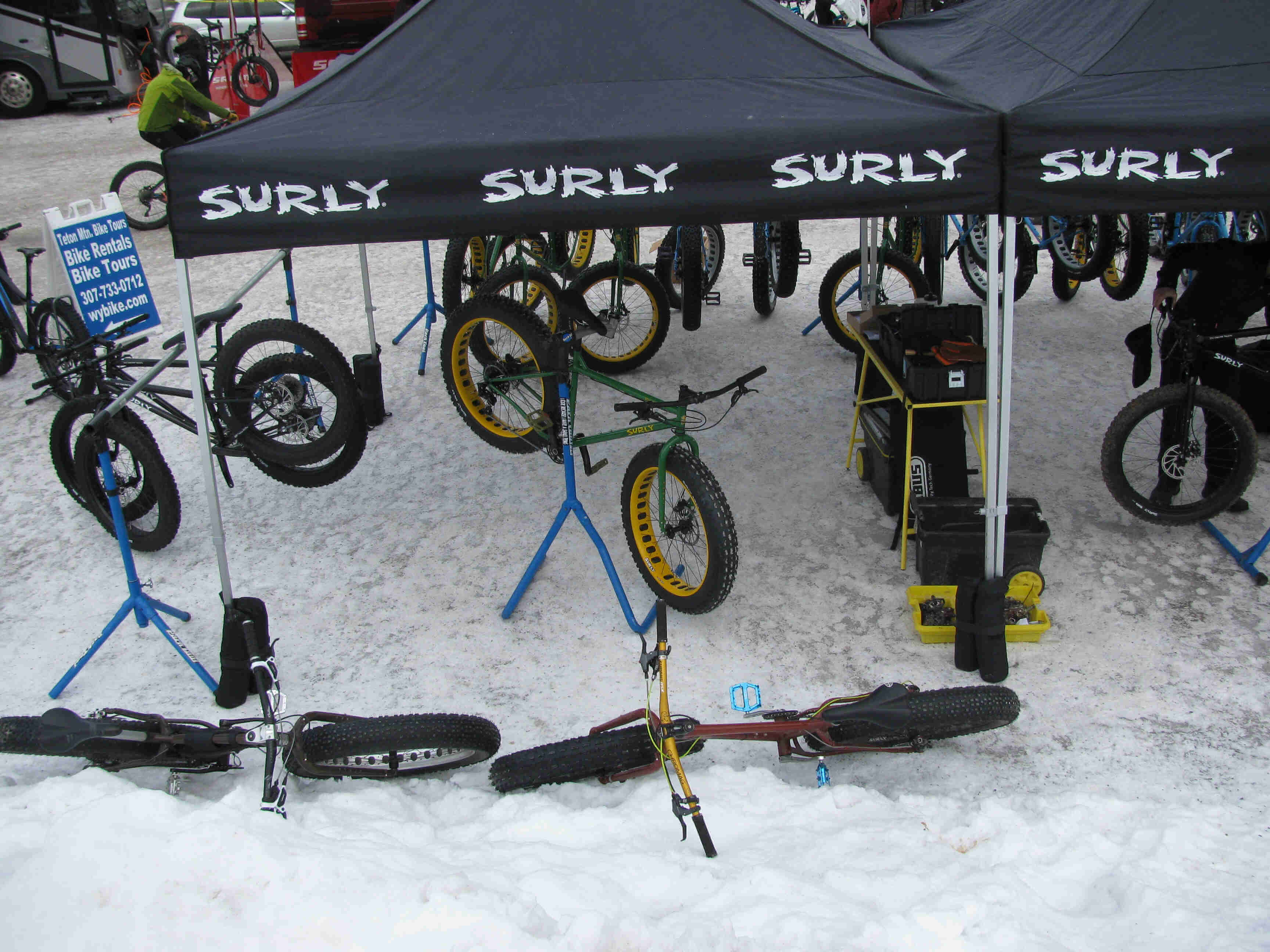 Downward view of a green Surly Ice Cream Truck fat bike on a stand, under a canopy in the snow, with fat bikes around