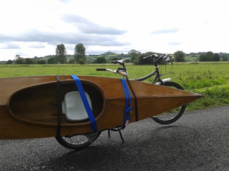 Right side view of a Surly Big Dummy bike with a wooden kayak strapped to the right side, with a field in the background